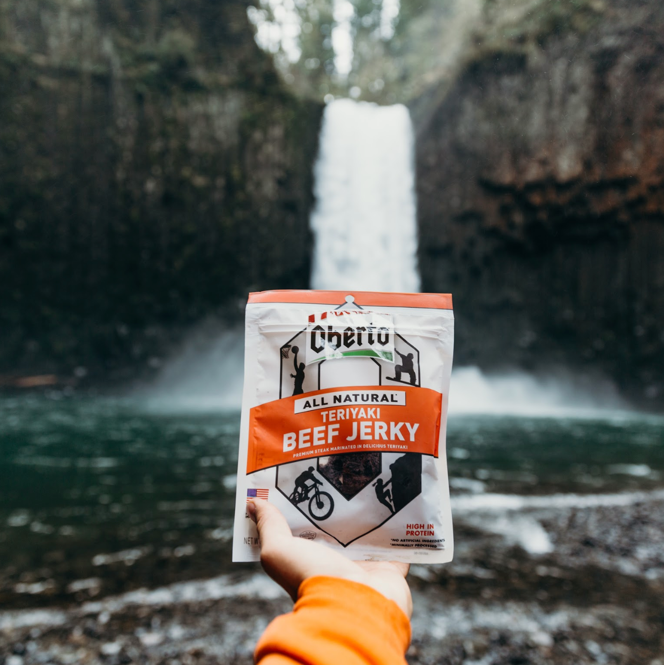 Oberto Jerky held out in front of a PNW waterfall