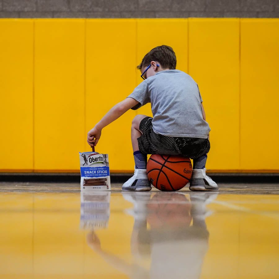 Young basketball player sits on his ball and enjoys Oberto Snack Sticks