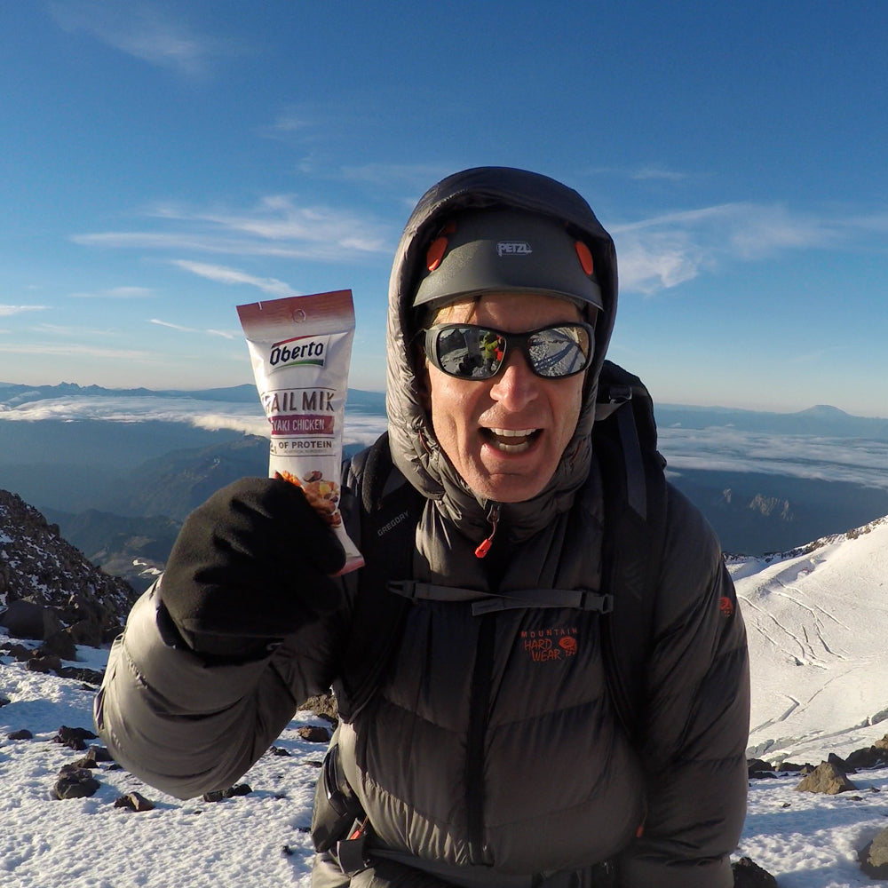 CEO, Tom Hernquist, poses for a photo with bag of trail mix near the top of Mount Rainier