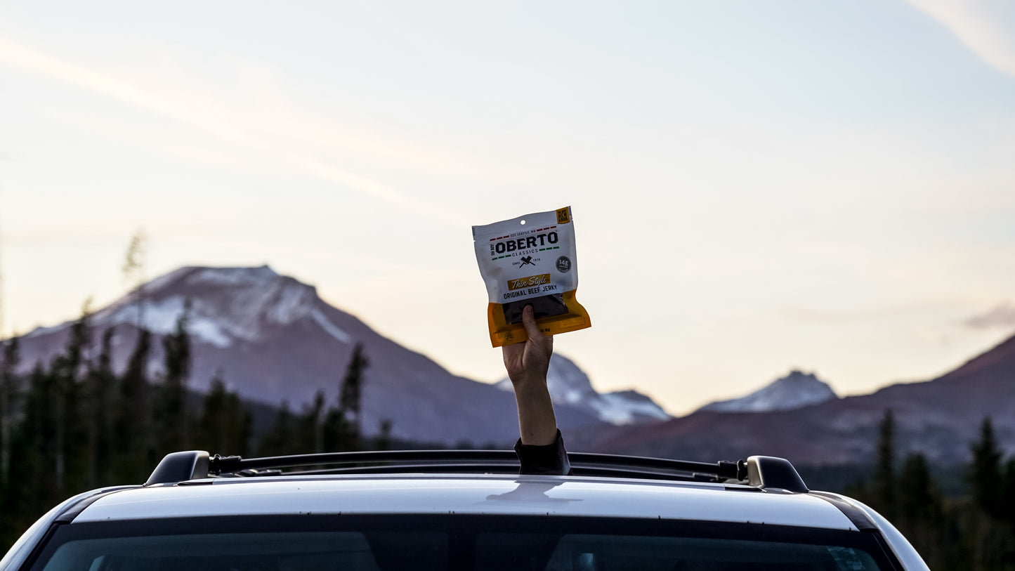 An extended hand holding a bag of Thin Style Original Jerky high out of the sunroof of a Four Runner. 